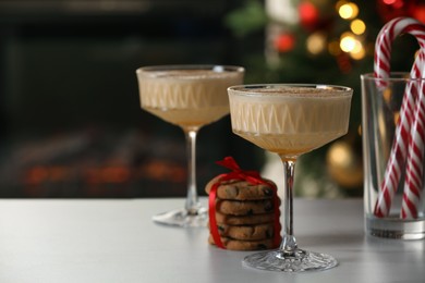 Photo of Tasty eggnog, cookies and candy canes on white marble table against blurred festive lights. Space for text