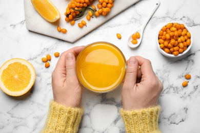 Photo of Woman with cup of fresh sea buckthorn tea at white marble table, top view