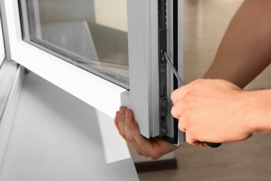 Photo of Worker adjusting installed window with screwdriver indoors, closeup