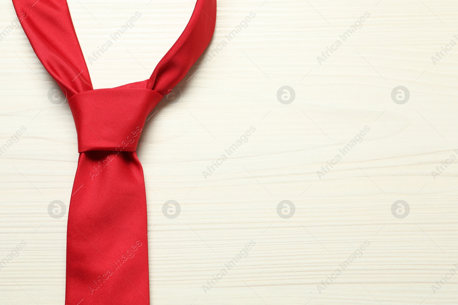 Photo of One red necktie on white wooden table, top view. Space for text