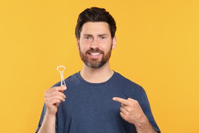 Happy man showing tongue cleaner on yellow background
