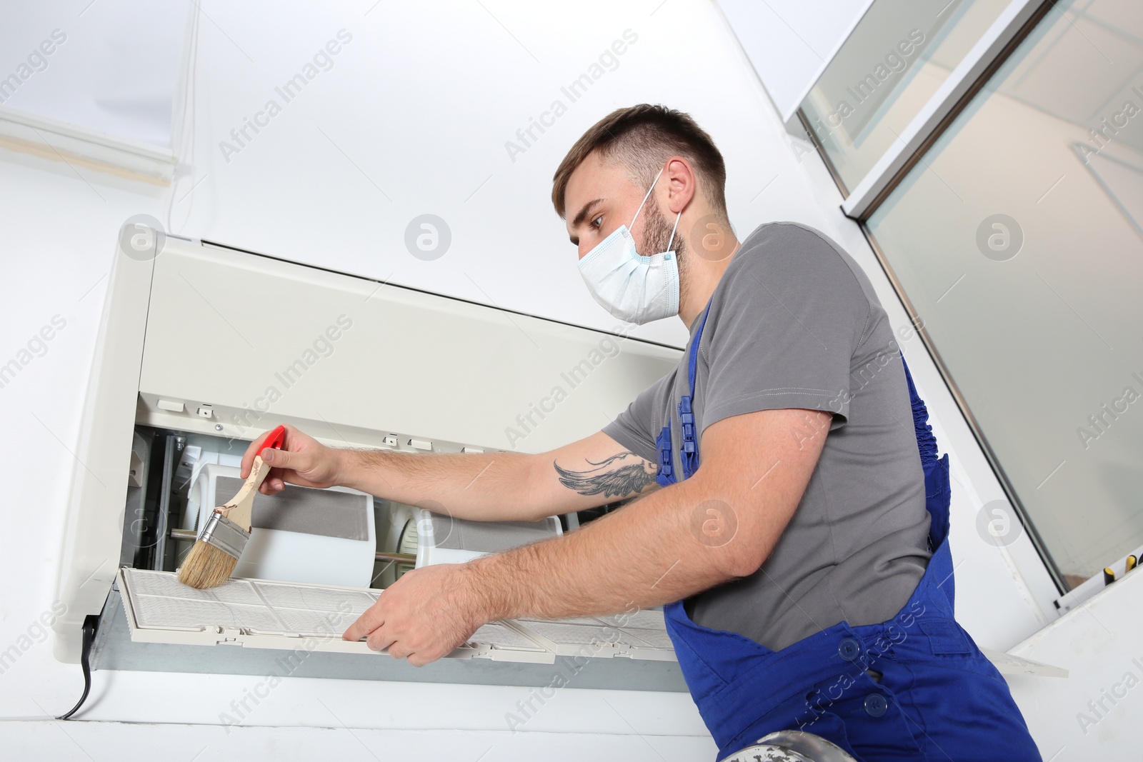 Photo of Young male technician cleaning air conditioner indoors