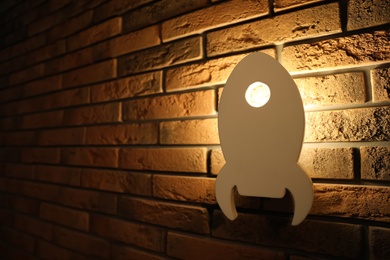 Photo of Rocket shaped night lamp on brick wall. Space for text