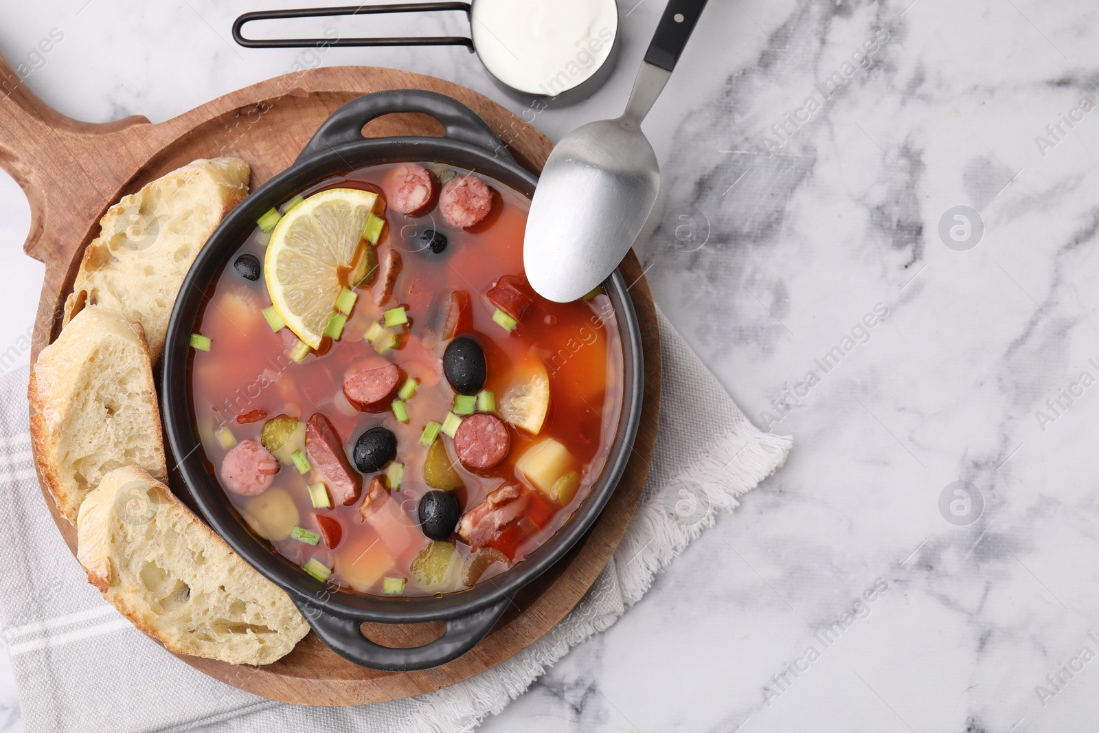 Photo of Meat solyanka soup with thin dry smoked sausages served on white marble table, flat lay. Space for text