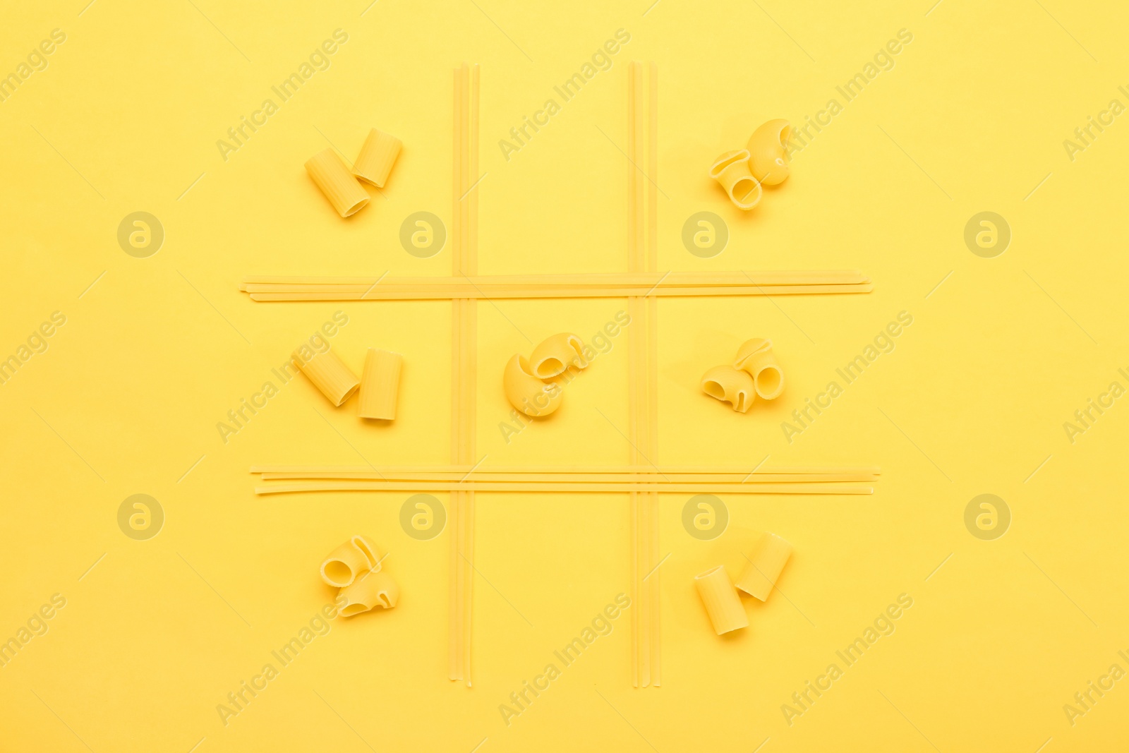 Photo of Tic tac toe game made with different types of pasta on yellow background, top view