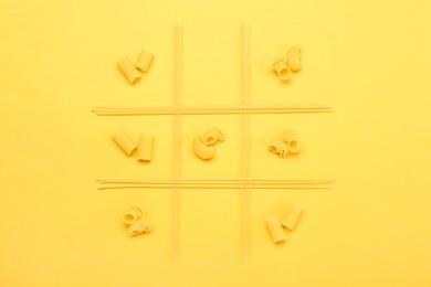 Tic tac toe game made with different types of pasta on yellow background, top view