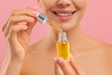 Young woman with serum in her hands on pink background, closeup