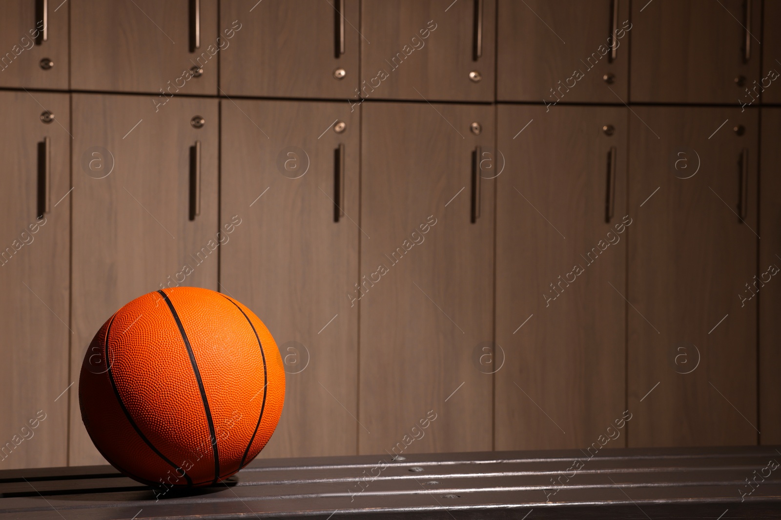Photo of Orange basketball ball on wooden bench in locker room. Space for text
