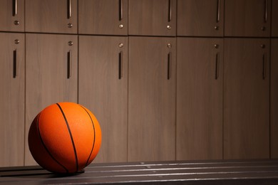 Photo of Orange basketball ball on wooden bench in locker room. Space for text