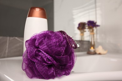 Photo of Purple shower puff and bottle of body wash gel on sink in bathroom, space for text
