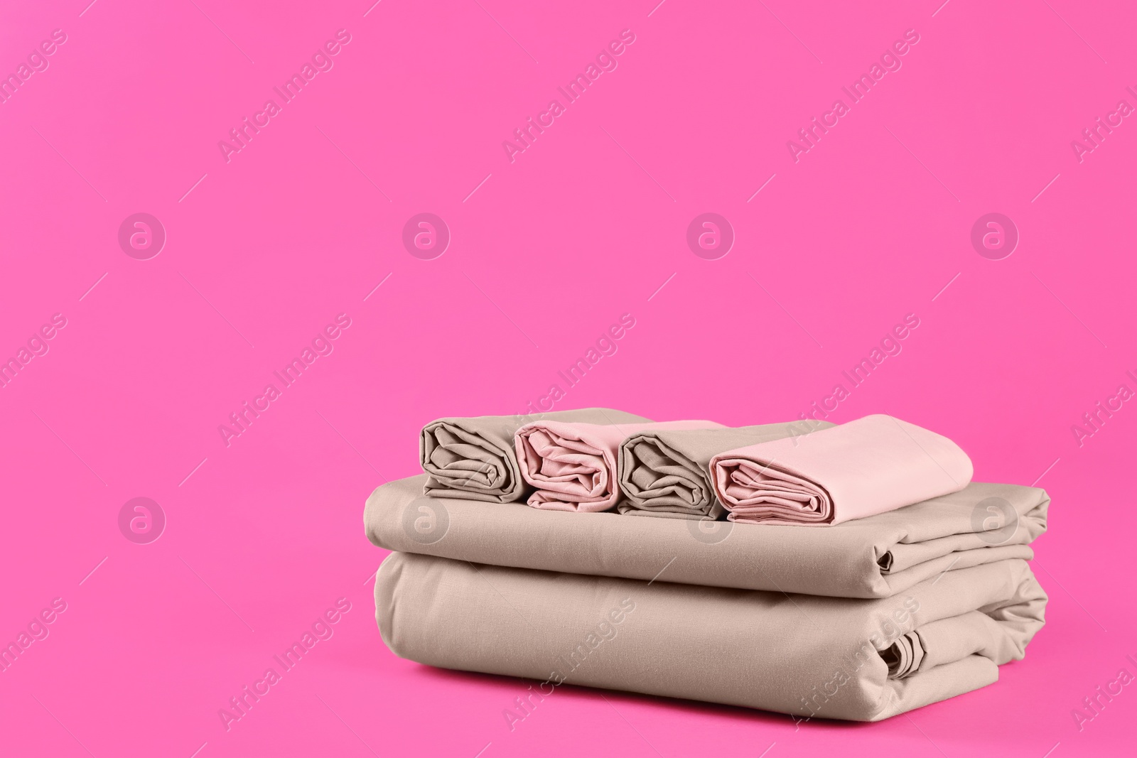 Photo of Stack of clean bed sheets on pink background. Space for text