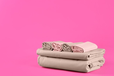 Stack of clean bed sheets on pink background. Space for text