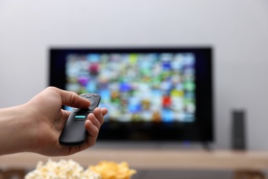 Woman switching channels on TV set with remote control at home, closeup. Space for text