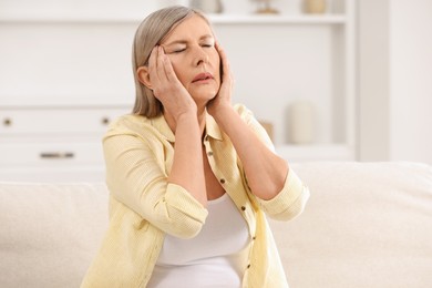 Photo of Menopause. Woman suffering from headache on sofa at home