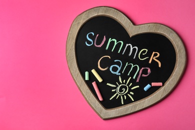 Heart shaped blackboard with text SUMMER CAMP, drawing and chalk sticks on color background, top view. Space for design