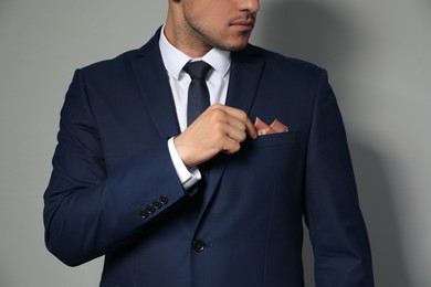 Man fixing handkerchief in breast pocket of his suit on light grey background, closeup