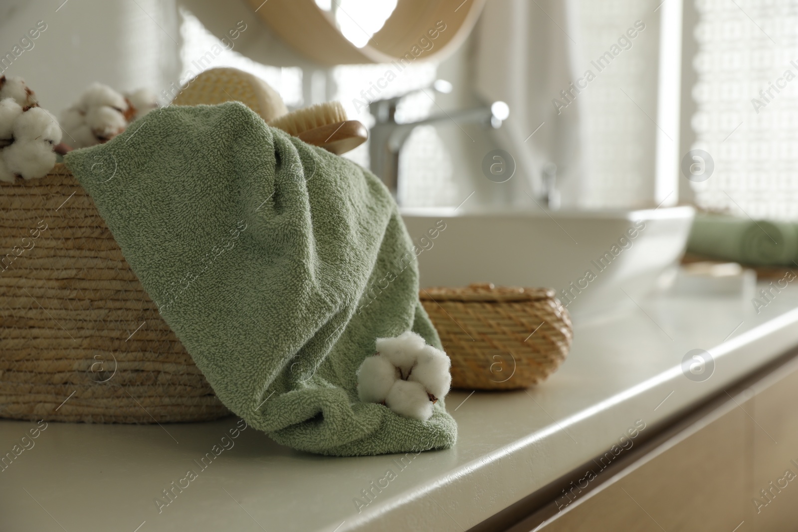 Photo of Wicker basket with clean towel, massage brush and cotton flowers on countertop in bathroom. Space for text