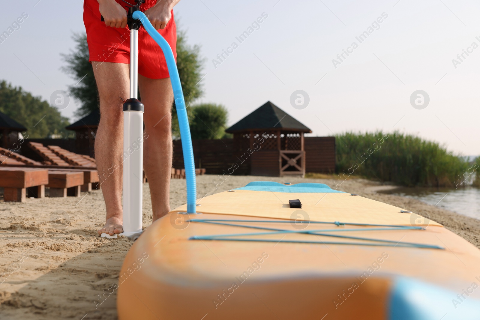 Photo of Man pumping up SUP board on river shore, closeup