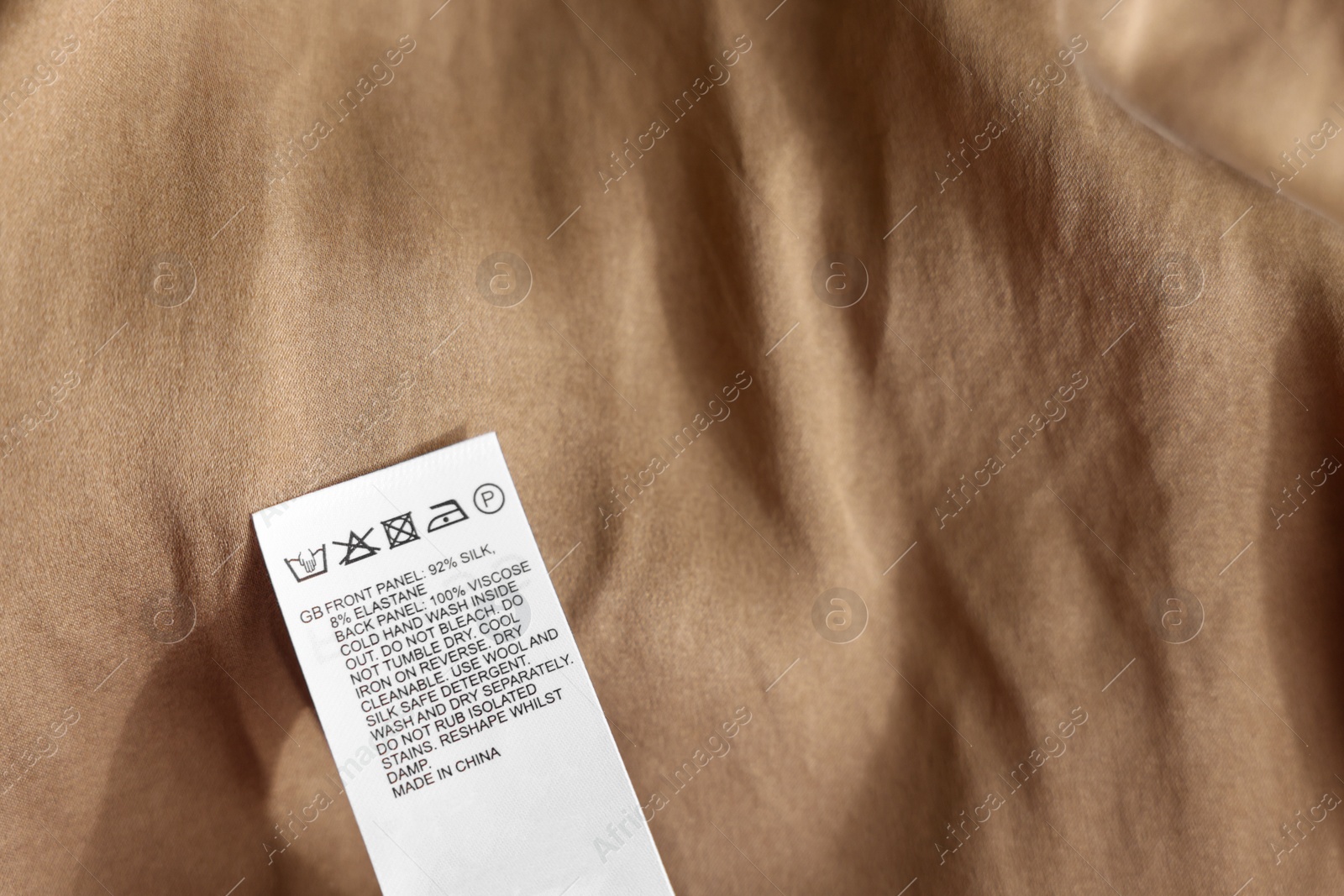 Photo of Clothing label in different languages on beige garment, closeup