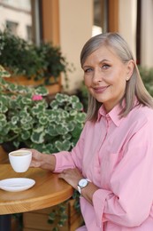 Photo of Portrait of beautiful senior woman drinking coffee at table in outdoor cafe