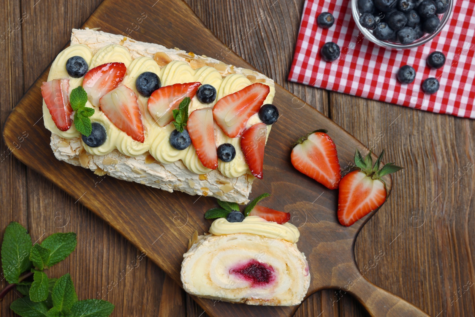 Photo of Tasty meringue roll with jam, cream, strawberry, blueberry and mint on wooden table, flat lay