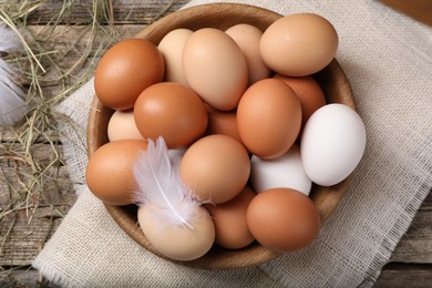 Photo of Fresh chicken eggs in bowl and dried hay on wooden table, flat lay
