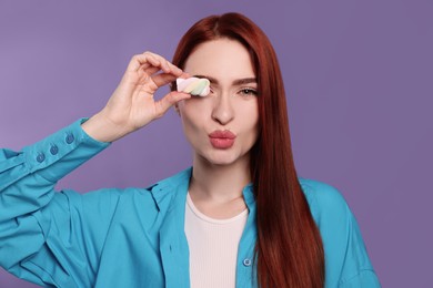 Photo of Beautiful woman with red dyed hair and marshmallow blowing kiss on purple background