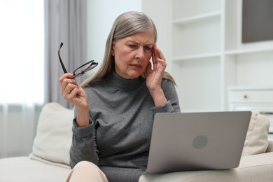 Overwhelmed woman with laptop sitting on sofa at home