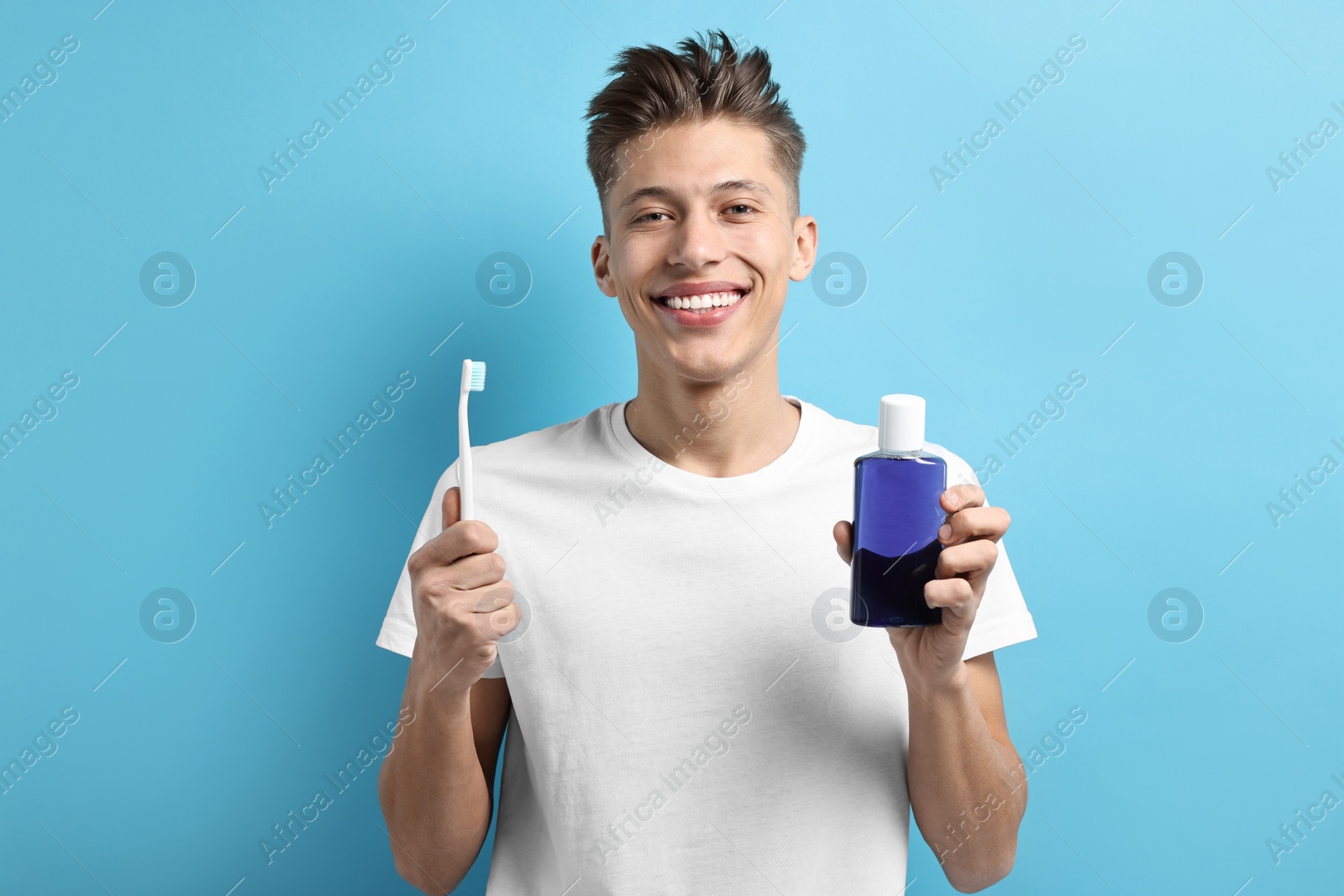 Photo of Young man with mouthwash and toothbrush on light blue background