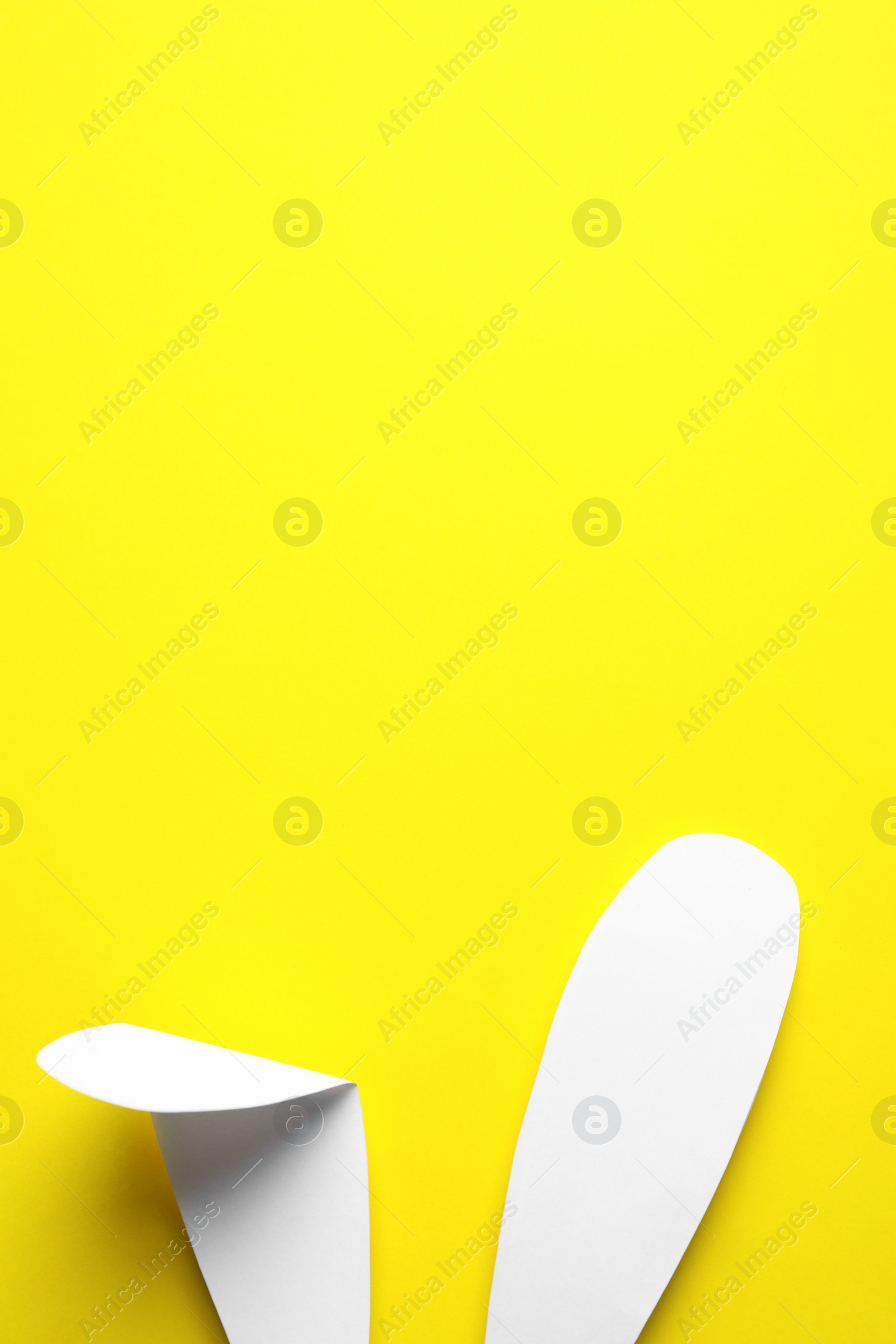 Photo of Top view of paper bunny ears on yellow background, space for text. Easter celebration