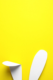 Photo of Top view of paper bunny ears on yellow background, space for text. Easter celebration