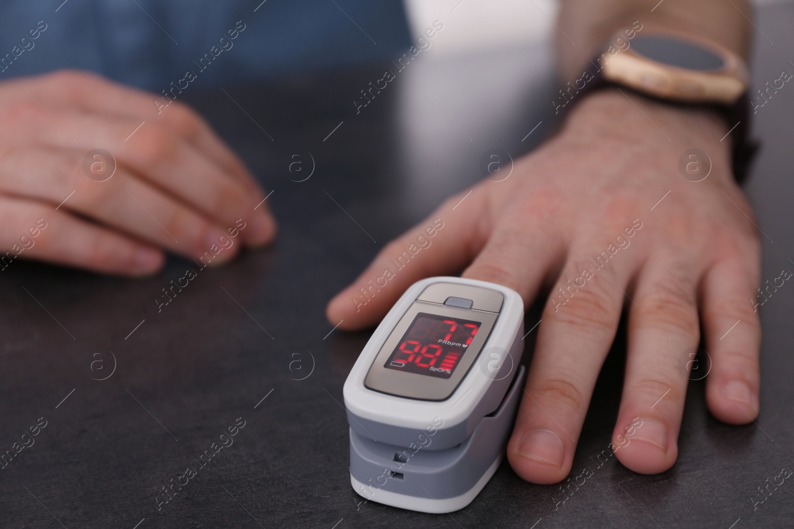 Photo of Man measuring oxygen level with modern fingertip pulse oximeter at grey table, closeup