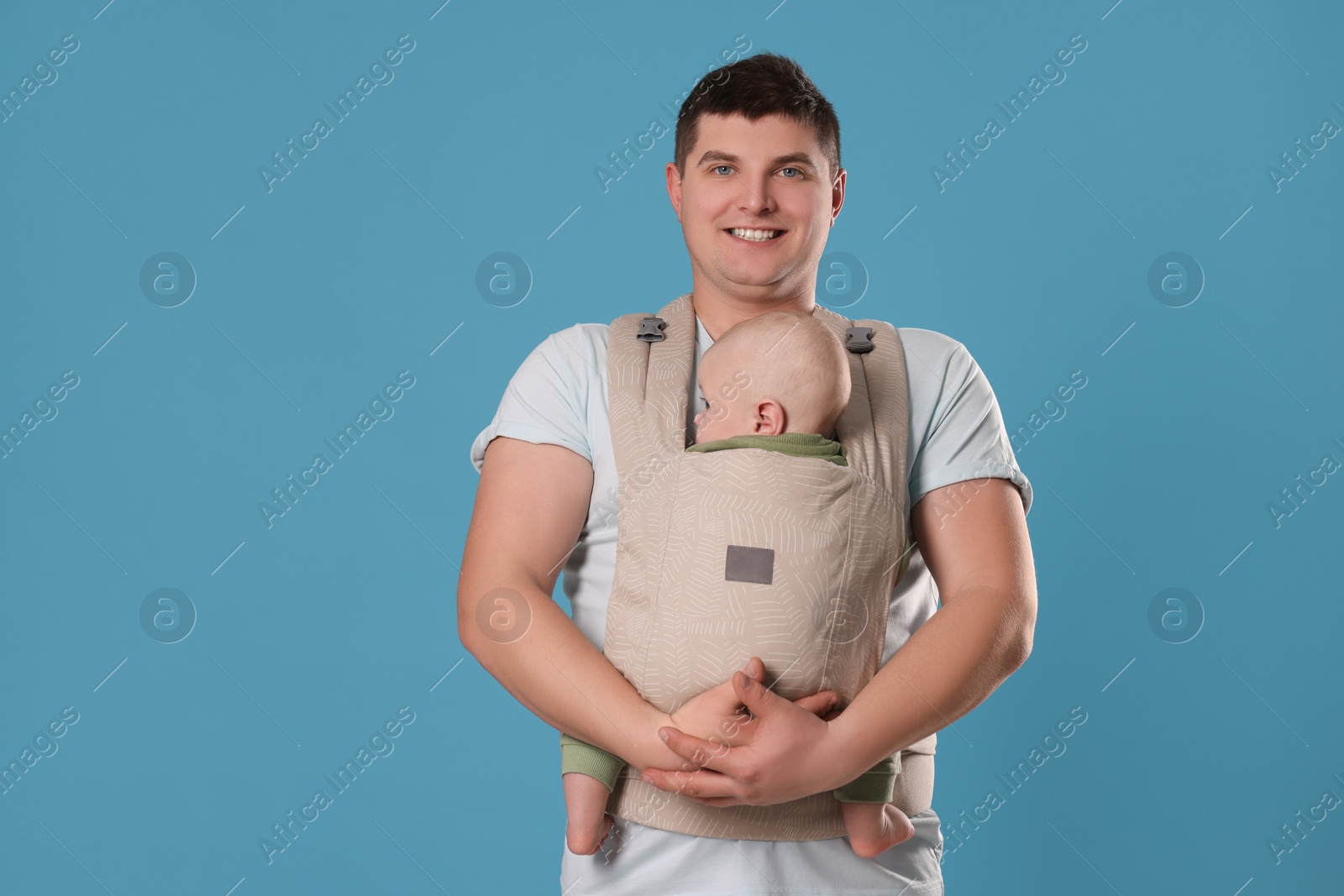 Photo of Father holding his child in sling (baby carrier) on light blue background