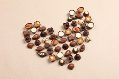 Photo of Heart made with delicious chocolate candies on beige background, top view