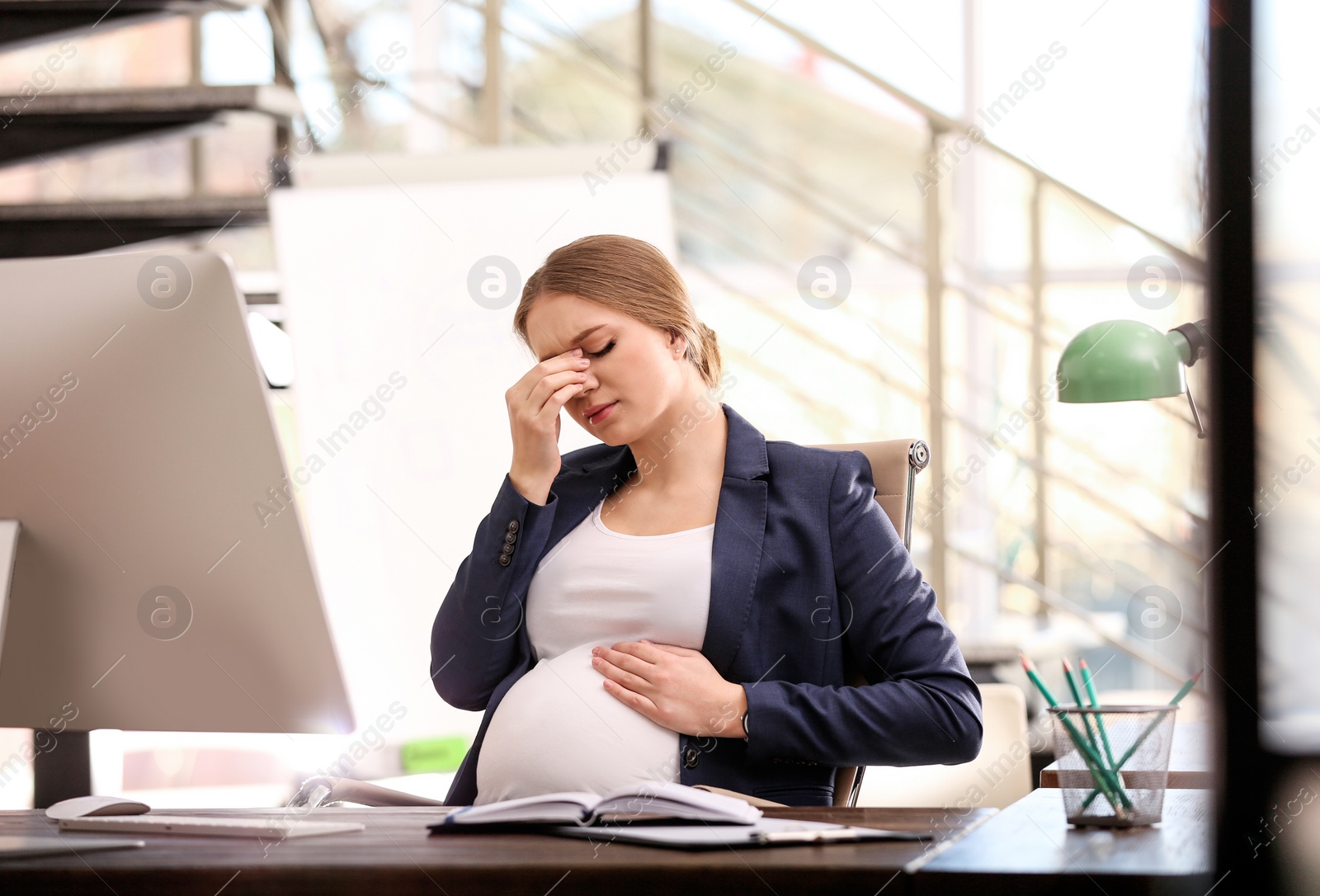 Photo of Young pregnant woman suffering from pain while working in office