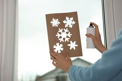 Woman using snow spray for decorating window with snowflakes at home, closeup