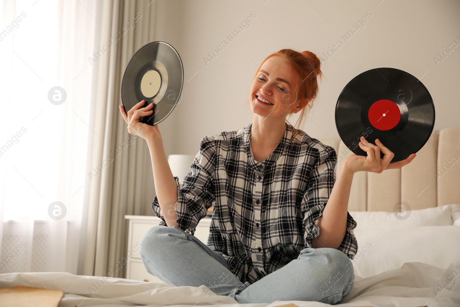 Photo of Young woman choosing vinyl disc to play music with turntable in bedroom