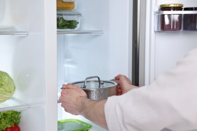 Photo of Man taking pot out of refrigerator in kitchen, closeup