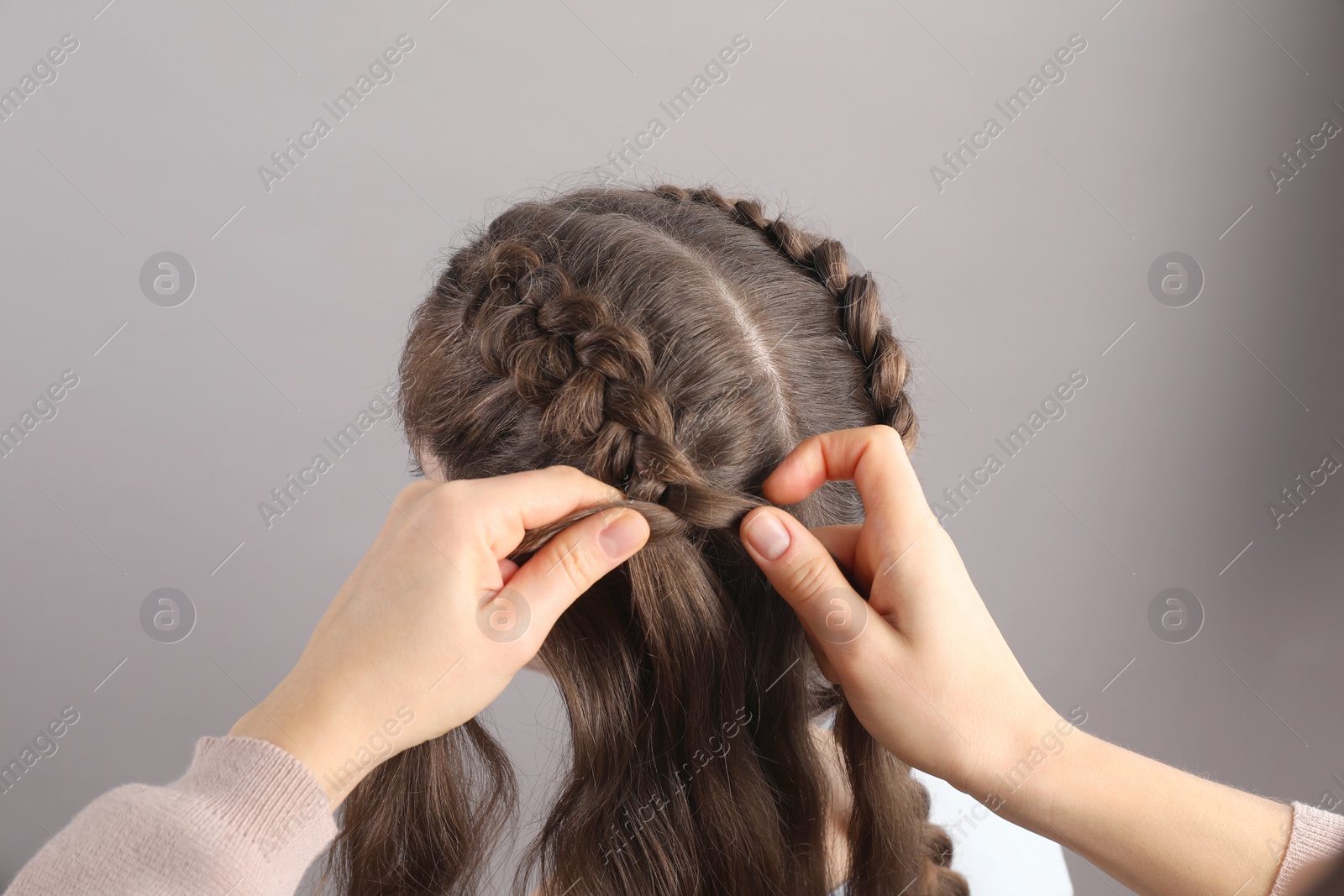 Photo of Professional stylist braiding woman's hair on grey background, closeup