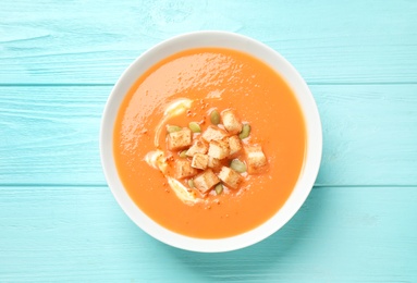 Photo of Tasty creamy pumpkin soup with croutons and seeds in bowl on light blue wooden table, top view