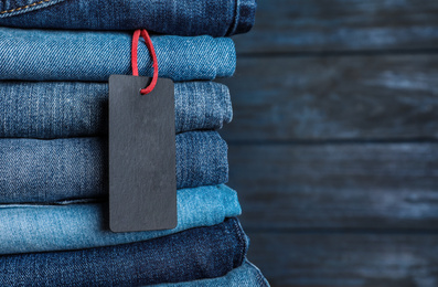 Stack of different jeans with tag on wooden background, closeup. Space for text