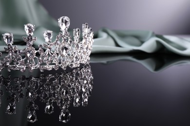 Beautiful silver tiara with gems near light cloth on dark mirror surface. Space for text