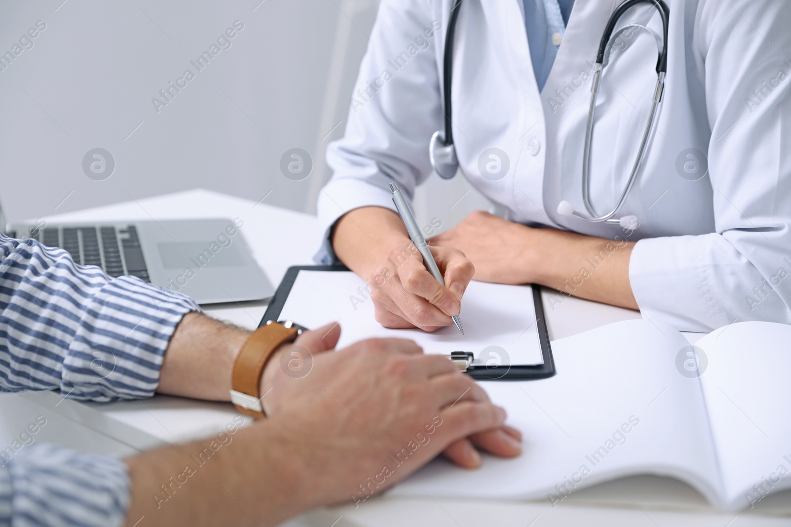 Photo of Doctor consulting patient at white table indoors, closeup