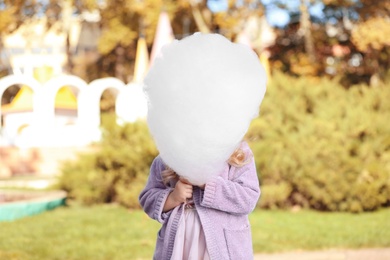 Photo of Cute little girl hiding behind cotton candy outdoors