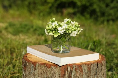 Photo of Book and glass with flowers on tree stump outdoors