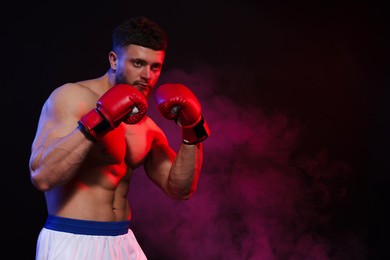 Photo of Man wearing boxing gloves on dark background. Space for text
