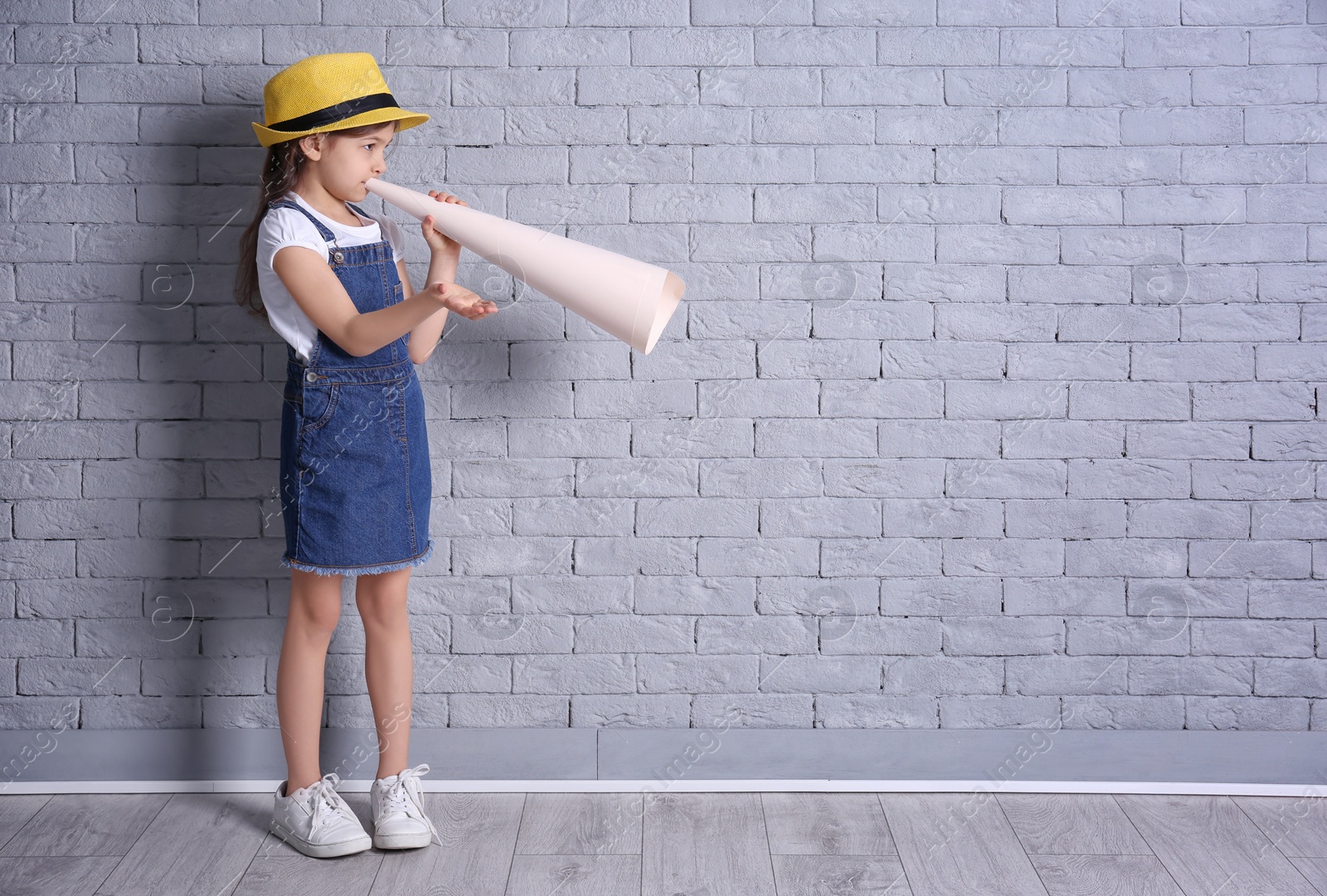 Photo of Adorable little girl with paper megaphone on brick wall background