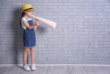 Adorable little girl with paper megaphone on brick wall background