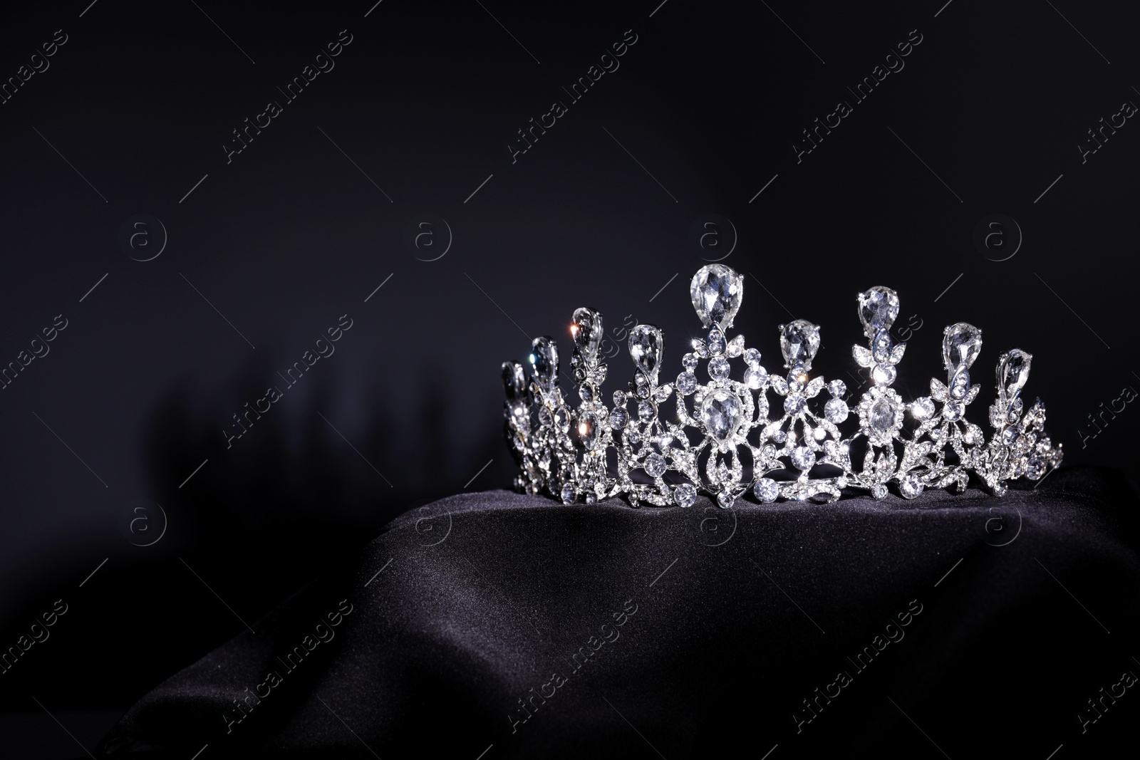 Photo of Beautiful silver tiara with diamonds on black cloth. Space for text