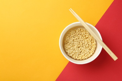 Cup of instant noodles with chopsticks on color background, top view. Space for text